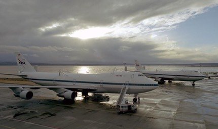 Two NASA Shuttle Carrier Aircraft parked on a wet ramp at sunset